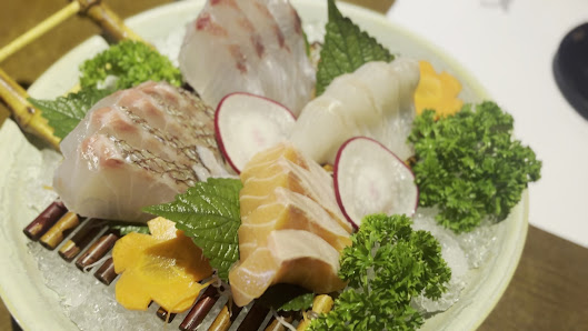 A plated dish of sashimi featuring various types of fish such as tuna and salmon, garnished with greens like radish slices and parsley leaves on a bed