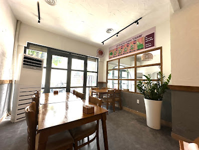 Interior space of a café/restaurant in Thao Dien, Saigon featuring wooden tables and chairs, large windows with natural light, a menu board on the wal