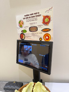 The image features a digital display (tablet) showing a menu interface with a person's reflection, mounted below a printed menu board. The menu board 