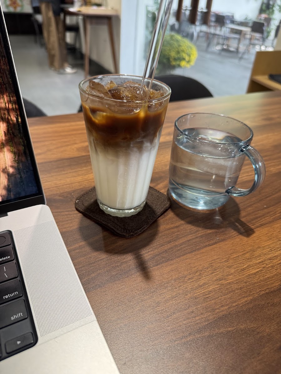 A close-up of a table in what appears to be an indoor cafe setting, featuring a glass with a layered drink and ice cubes on the left side, accompanied