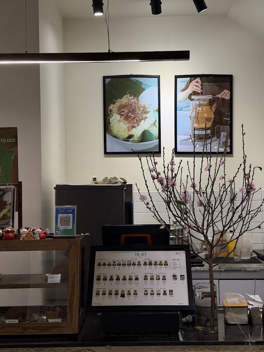 The image shows an interior view of a cafe or restaurant in Thao Dien, Saigon. The decor includes framed pictures on the wall depicting food items and