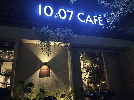 The image shows an exterior view of a café named '10.07 Café' at night time with illuminated signage above the entrance.