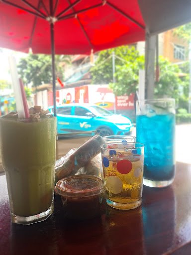 The image shows a table at an outdoor cafe setting in Thao Dien, Saigon with various drinks and condiments on it.