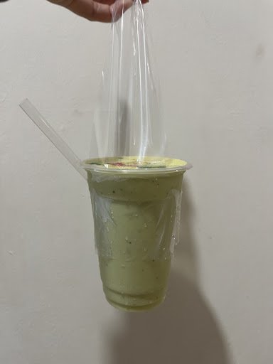 A close-up of a green-colored drink in a plastic cup with a straw and lid being covered by a transparent bag.