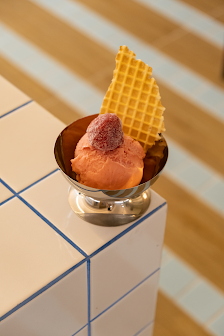 A dessert consisting of a scoop of pink ice cream topped with what appears to be a berry compote or sauce in a small, shiny metallic bowl on top of a