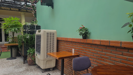 An outdoor seating area of a venue in Thao Dien, Saigon, featuring a green wall with a brick base, wooden tables, a purple chair, potted plants, and a