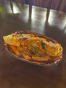 A plated dish consisting of a rolled omelet garnished with green onions and possibly other vegetables or meats in sauce, served on an ornate plate.