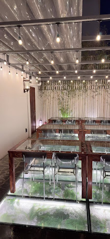 The image depicts an indoor space that appears to be a modern and stylish venue with multiple tables set up on what looks like glass platforms over wa