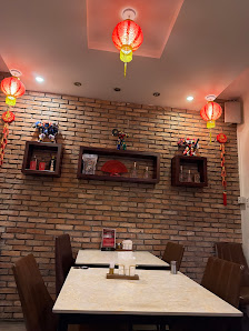 A restaurant interior featuring exposed brick walls, wooden chairs, and tables with condiment containers. Decorative elements include red lanterns han
