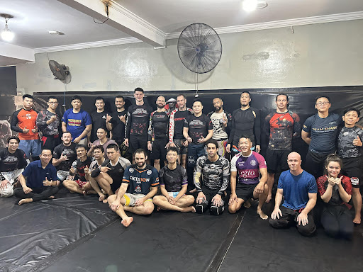 A group of individuals is gathered in a martial arts training session or seminar. They are wearing various styles of athletic wear and some have logos