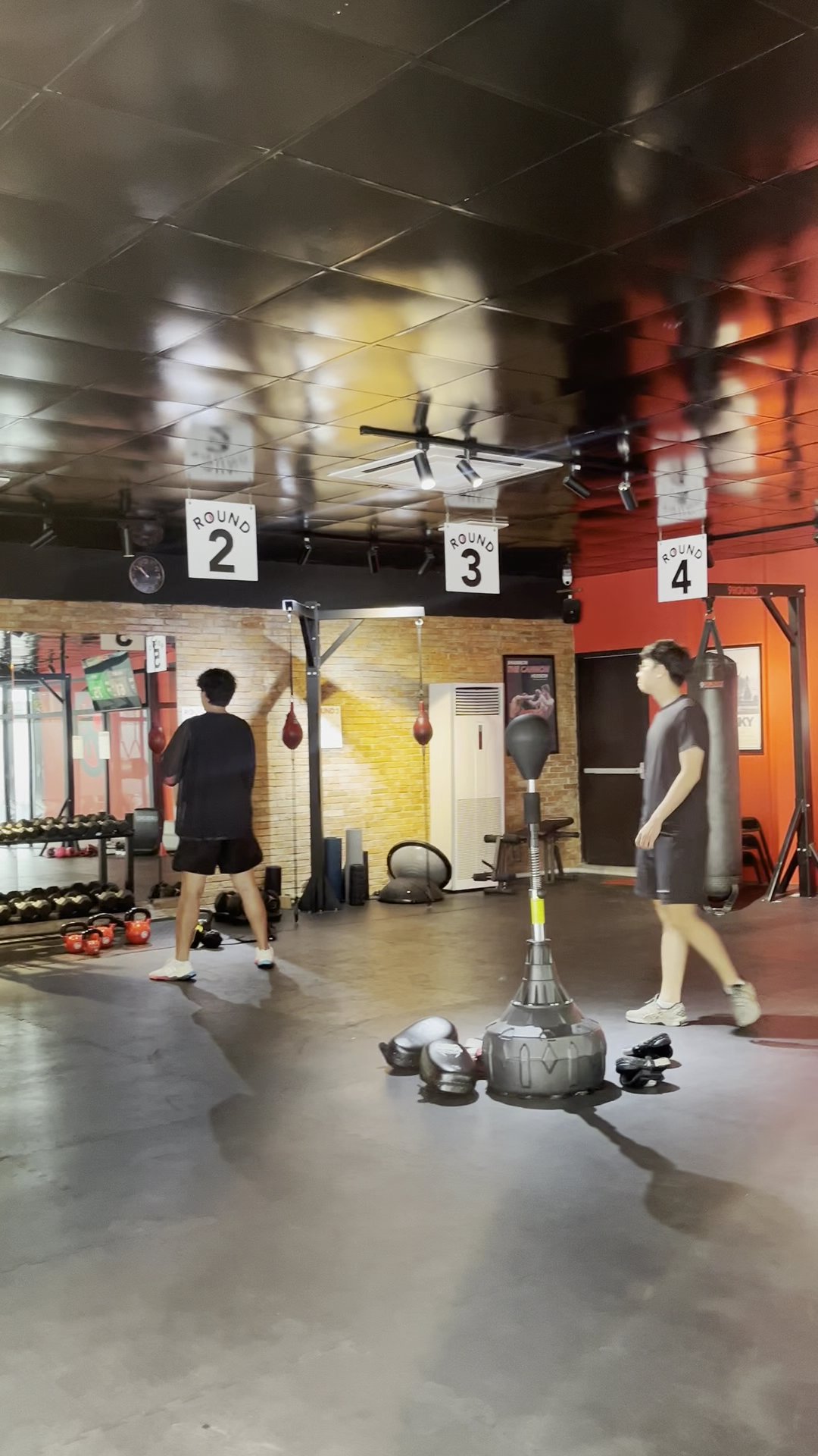 The image depicts the interior of a boxing gym located in Thao Dien, Saigon. Two individuals are present, one facing away and the other walking. The s