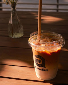 A close-up shot of a cold beverage in a plastic cup from 'Thao Dien Cafe', featuring an orange-colored drink with visible ice cubes and a straw.