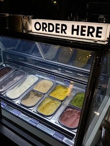 The image shows a display case in an ice cream shop where various flavors of soft-serve ice cream are available for order.