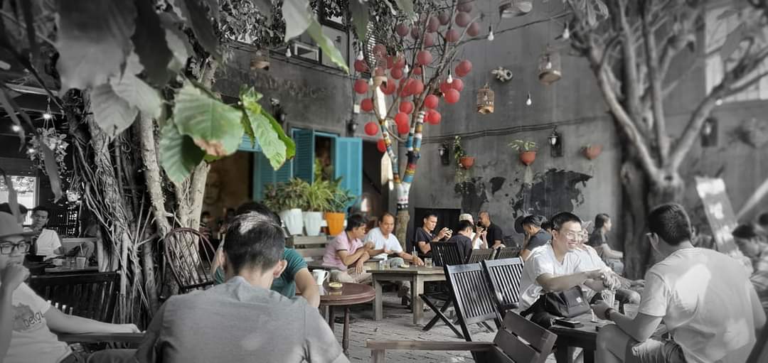The image depicts an interior scene of a casual dining establishment in Thao Dien, Saigon. The setting is filled with patrons seated at tables engaged