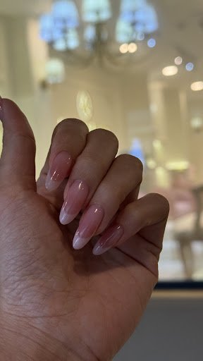 A close-up of a person's hand displaying manicured nails painted in a pinkish nude shade with French tips. The background is blurred but suggests an u