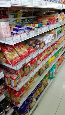 The image shows a well-stocked grocery shelf in an aisle of a supermarket or convenience store with various packaged food items such as bread, snacks,