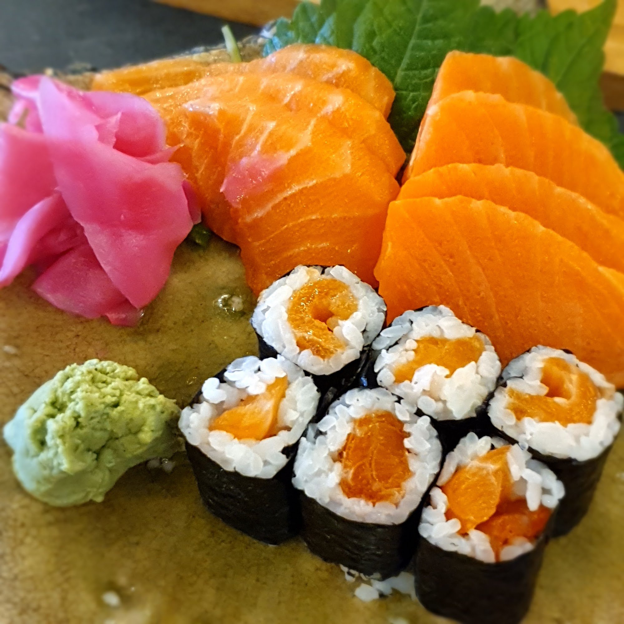 A plate of sushi and sashimi featuring salmon nigiri, ahi tuna rolls with orange roe, green wasabi paste, pickled ginger, and seaweed-wrapped pieces t