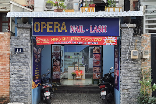 The image shows an exterior view of a nail and lash salon named 'Opera'. The entrance is marked by a blue awning with the business name in bold white 