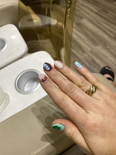 A close-up of a person's hand displaying variously painted nails and rings on their fingers resting on what appears to be the armrest of an airplane s