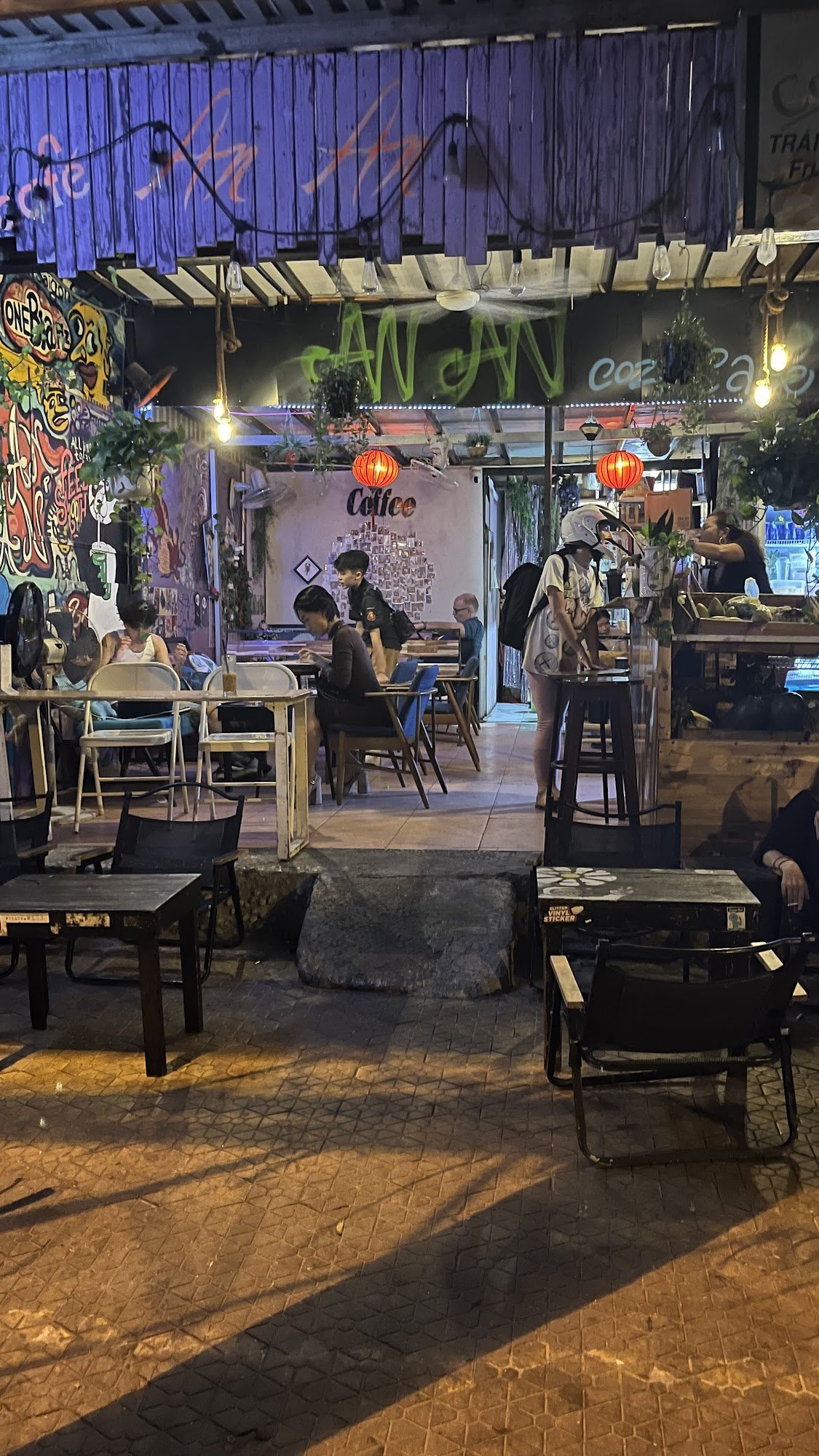 The image depicts an outdoor seating area of a café at night. The establishment is named 'Café Coffee Day' and features various decorations including 