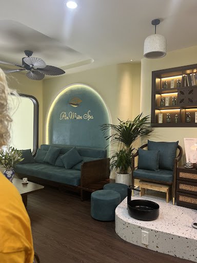 The image shows an interior space of a spa named 'Anh Mien Spa'. It features teal-colored seating with cushions, green plants in the background and on