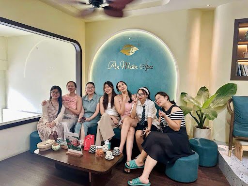 A group of seven women is seated in a spa setting at Thao Dien Spa. They are posing for the camera with smiles, surrounded by various items such as cu