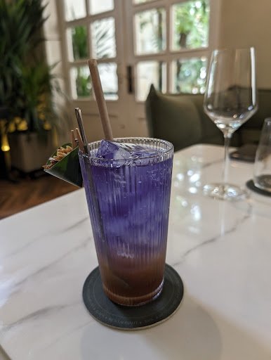 A layered cocktail in a tall glass with purple and brown layers, garnished with a chocolate wafer stick on the rim and ice cubes inside.