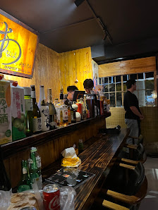 The image shows an interior view of a bar or restaurant at night time. The counter is well-stocked with various bottles and glasses, indicating it's r