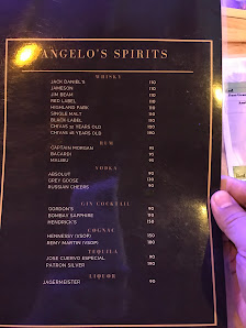 A menu from a venue named 'Angelo's Spirits' is displayed on a table with dim lighting and someone holding the page.