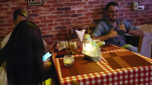 A group of people sitting at a table in an indoor setting that appears to be a restaurant or cafe with brick walls and red checkered tablecloths.