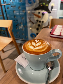 A close-up shot of a latte art on top of a cup of coffee in an indoor setting with modern decor, including a blue and white snowman design visible thr