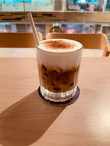 A glass of cold coffee beverage topped with a layer of milk foam and sprinkled with cocoa powder on top.