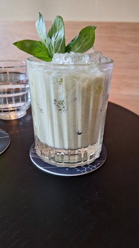 A close-up of a refreshing drink in a glass filled with ice and garnished with fresh basil leaves on top.