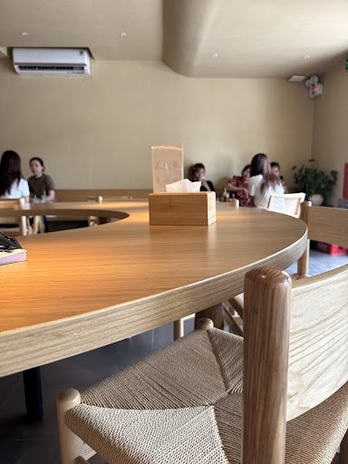 The image shows an interior view of a modern cafe or restaurant with wooden furniture and beige walls. A large table is in the foreground, featuring w