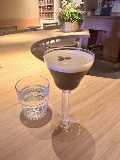 A close-up of a glass containing an espresso-based beverage on a wooden table in what appears to be the interior of Thao Dien, Saigon.