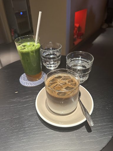 The image shows a table setting in what appears to be an indoor venue, possibly a café or restaurant. On the table are two glasses of green smoothie w