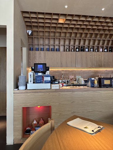 The image shows a modern interior of what appears to be a coffee shop or bar with wooden shelves and counters displaying various items such as bottles