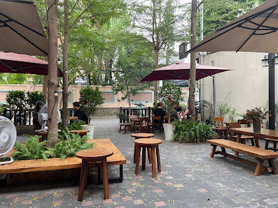 The image shows an outdoor seating area of a cafe or restaurant in Thao Dien, Saigon. There are several wooden tables and benches under large red umbr