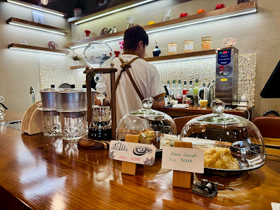 The image shows an interior view of a cafe or bar counter area where drinks and snacks are displayed under glass domes, with various bottles on the sh