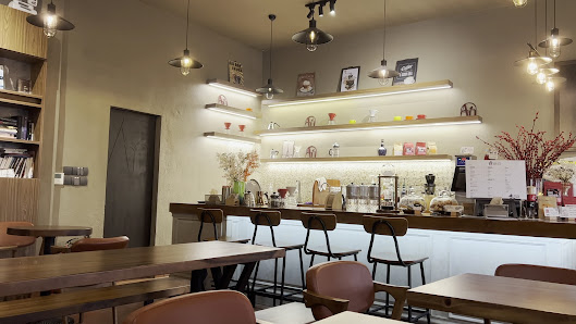 This image depicts an interior view of a modern café or coffee shop. The space is well-lit with warm lighting, featuring wooden tables and chairs in t