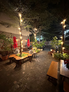 The image depicts an outdoor seating area of a restaurant or cafe at night time. The space is illuminated by string lights draped around trees and han