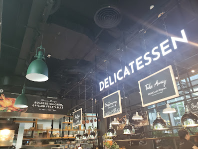 The image depicts the interior of a modern café or deli in Thao Dien, Saigon. Prominent signage includes "DELICATESSEN" in large illuminated letters, 