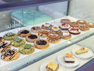 A display case in a venue showcasing an assortment of desserts and pastries such as cookies, cakes, tarts, and cheesecakes with various toppings like 