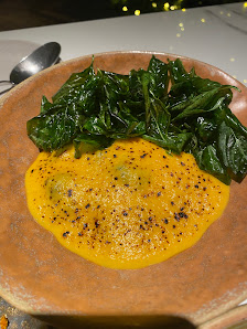 A plated dish featuring a vibrant yellow puree topped with dark green leafy greens on an earth-toned plate.