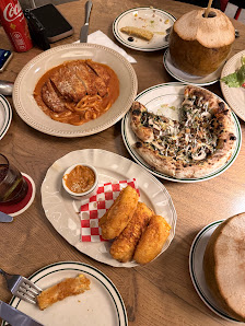 A table filled with various dishes including a bowl of spaghetti in tomato sauce, a pizza topped with mushrooms and cheese, fried chicken nuggets on a