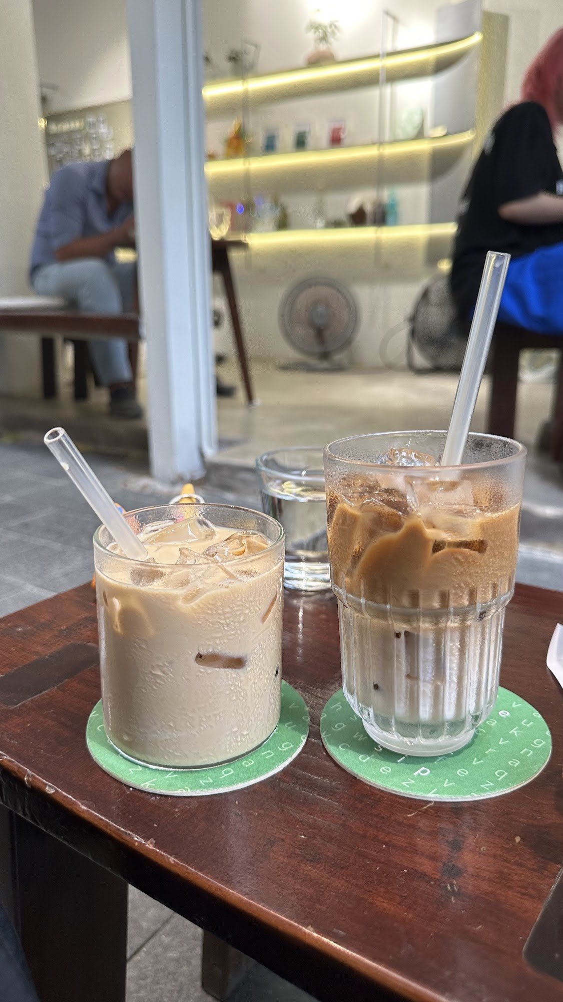Two glasses of cold beverages on a table in an indoor setting that appears to be a café or restaurant.