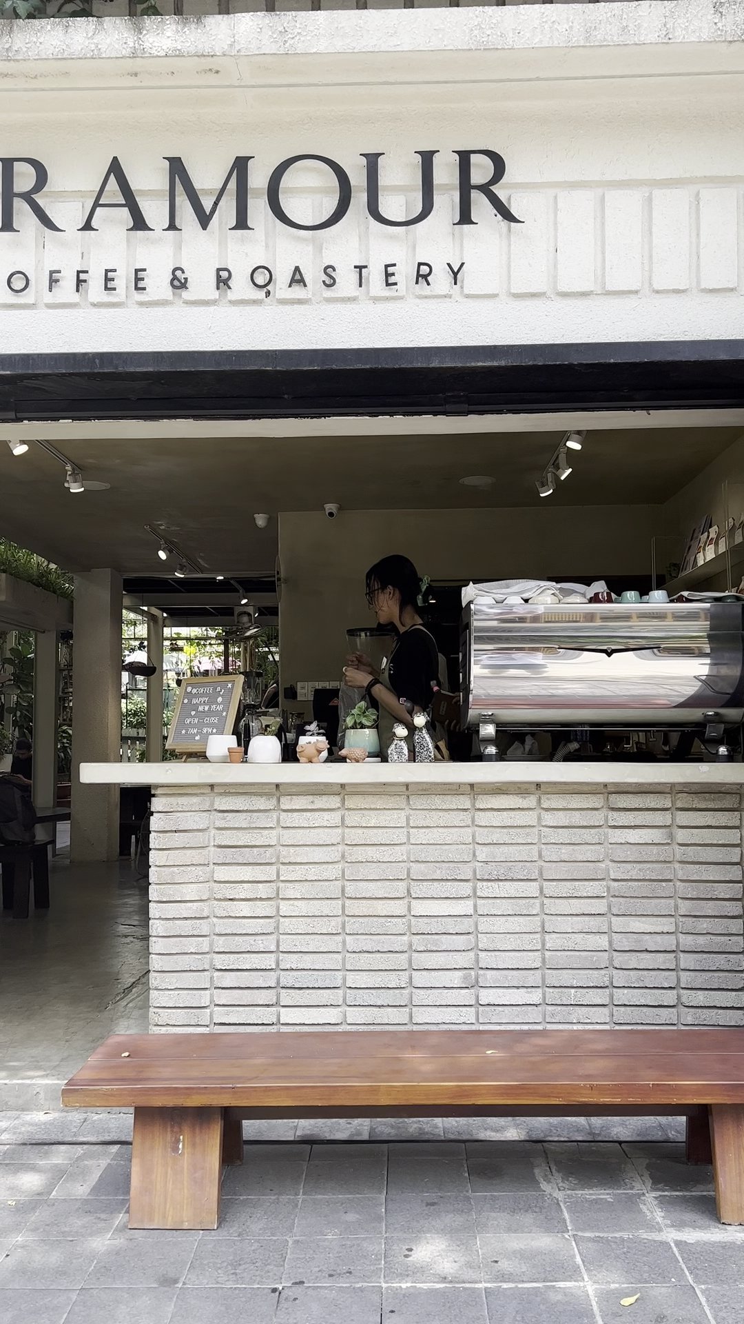 The image shows an interior view of a coffee shop named 'RAMOUR COFFEE & ROASTERY'. The establishment has a modern and clean design with white brick w