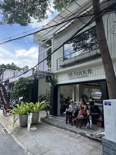 The image shows an exterior view of a coffee shop named 'ARMOUR,' which appears to be located in Thao Dien, Saigon. The establishment has large window