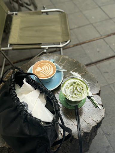 A close-up view of a table outside an establishment displaying two beverages: one appears to be a latte with artful foam design on top, served in a bl