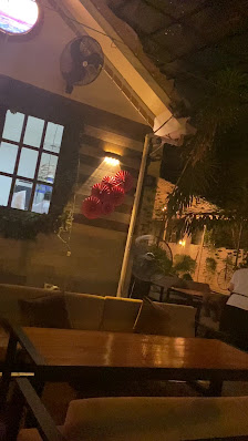 The image shows an interior view of a restaurant or cafe at night time. The focus is on the wooden tables and chairs in the foreground, with dim light